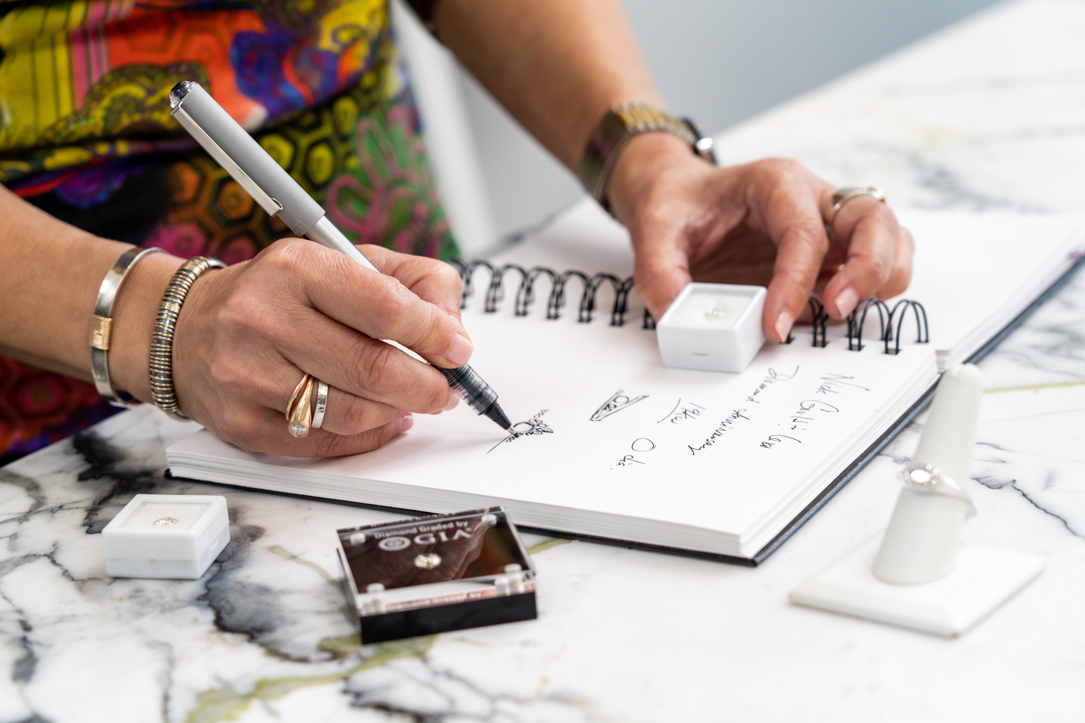 Kathryn sketching a jewelry design and examining diamonds, highlighting the custom creation process.